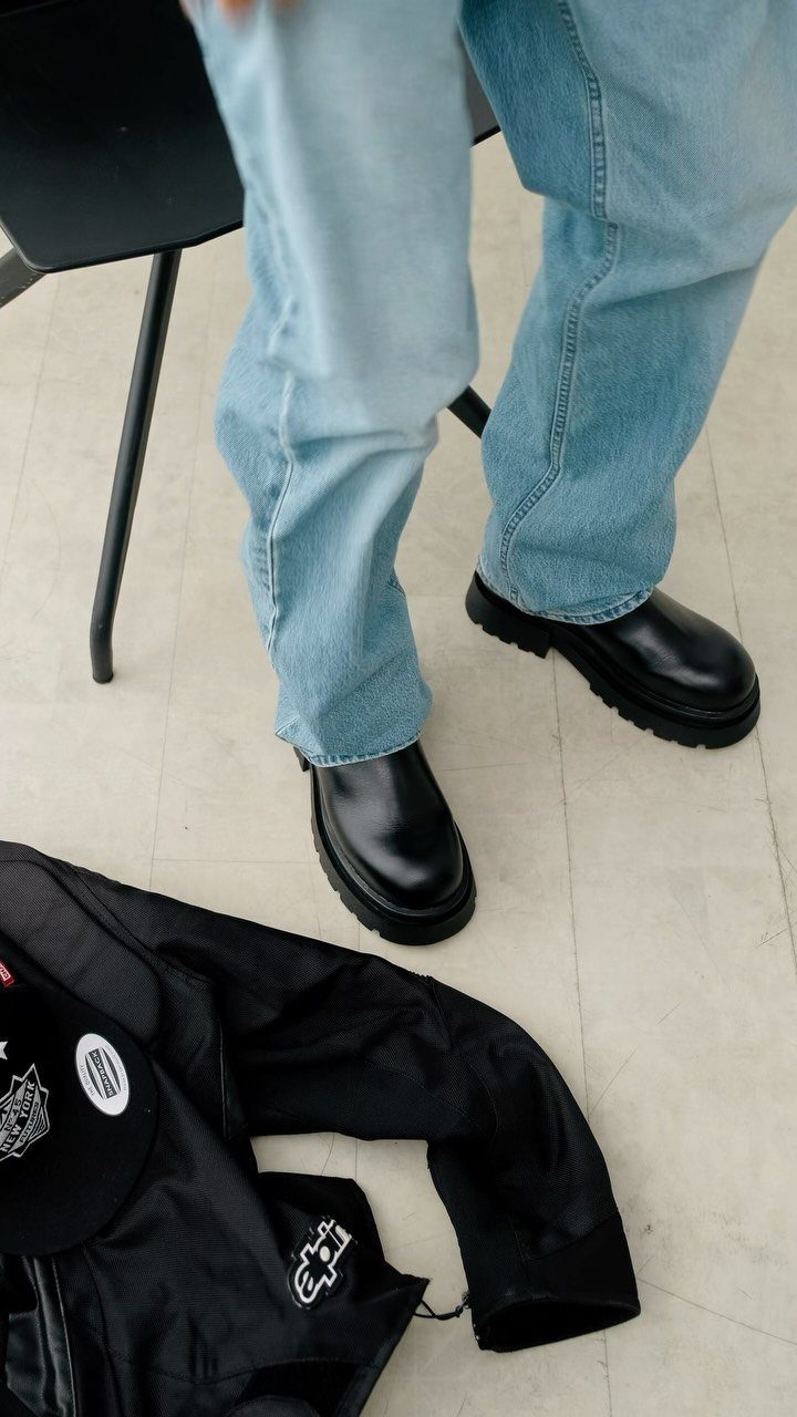 Light blue jeans paired with chunky black leather chelsea boots on a light floor.