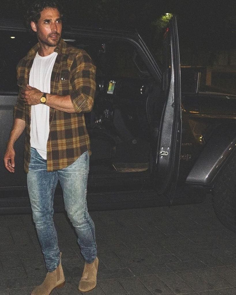 Man wearing brown plaid shirt, blue jeans, and tan suede Chelsea boots.
