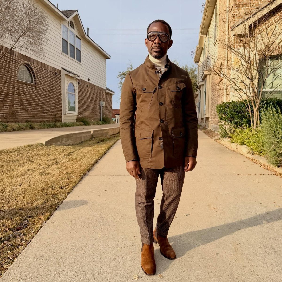 Man wearing a brown field jacket, patterned trousers, and tan suede Chelsea boots.