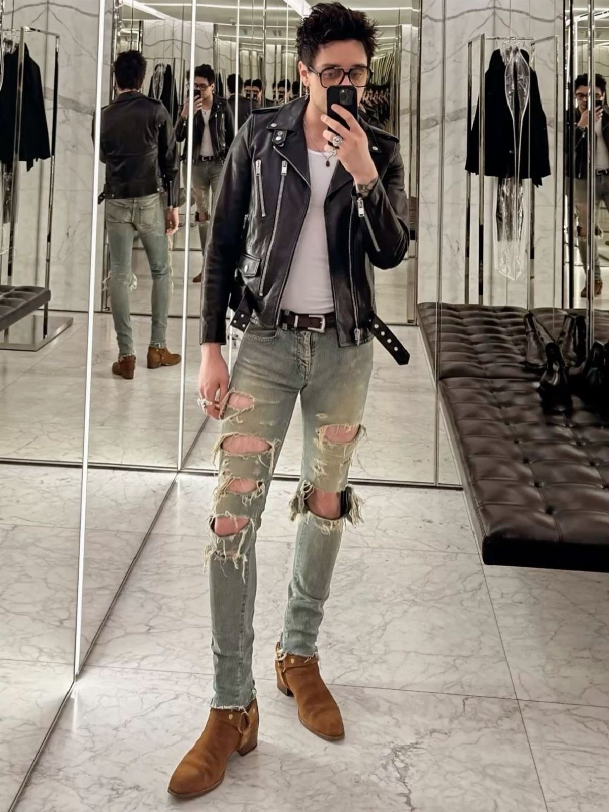 Man wearing a black leather jacket, ripped light blue jeans, and brown chelsea boots.