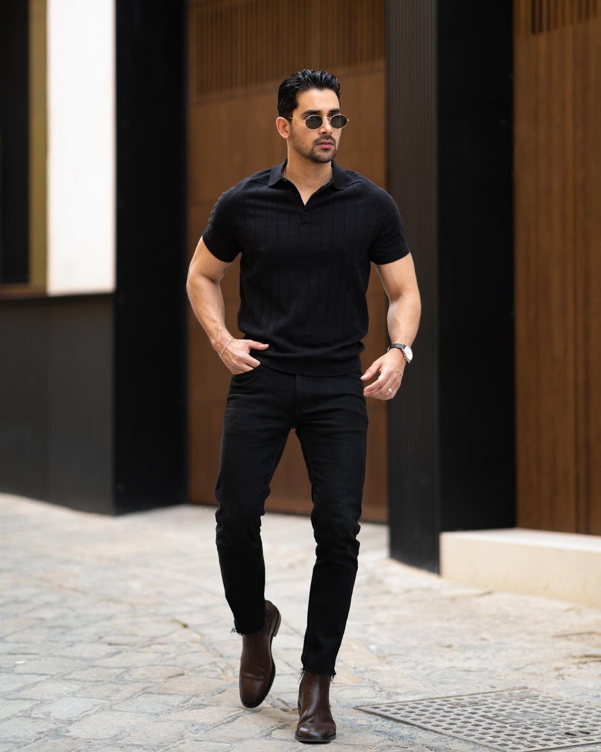 Man in black polo shirt and black trousers wearing dark brown leather Chelsea boots.