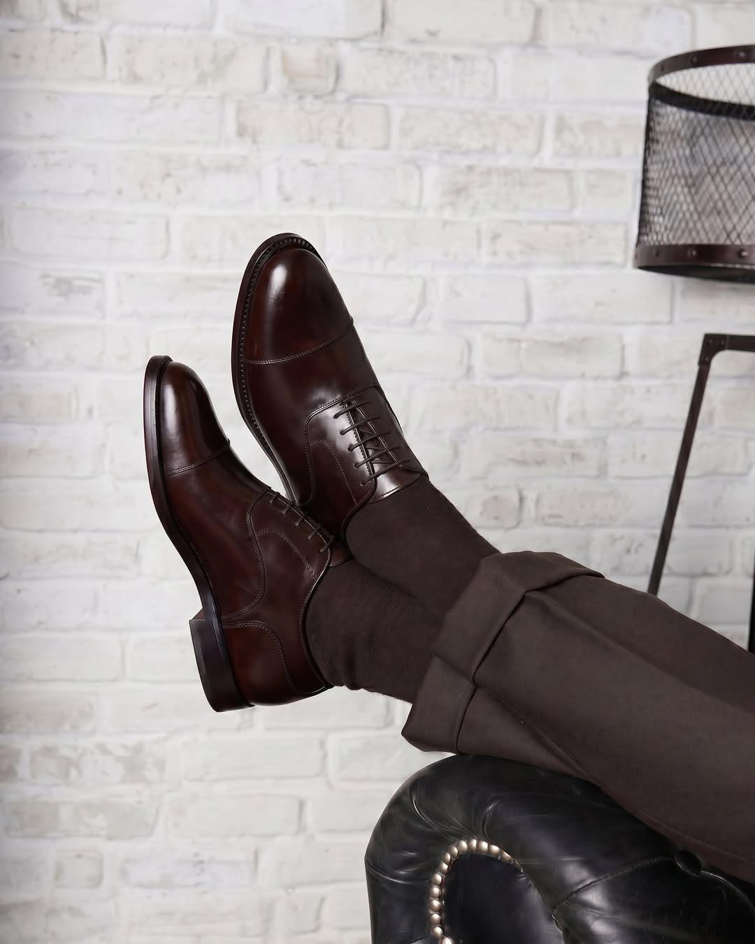 Dark brown leather oxford shoes paired with brown trousers and socks.