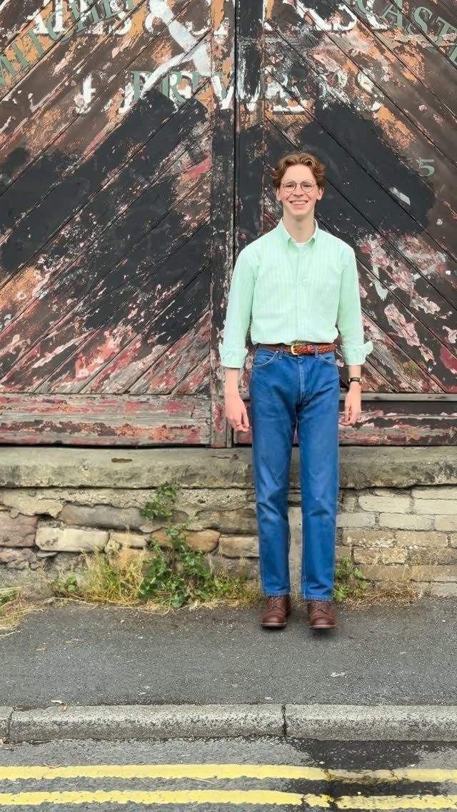 Man wearing a light green shirt, blue jeans, and brown oxford shoes.