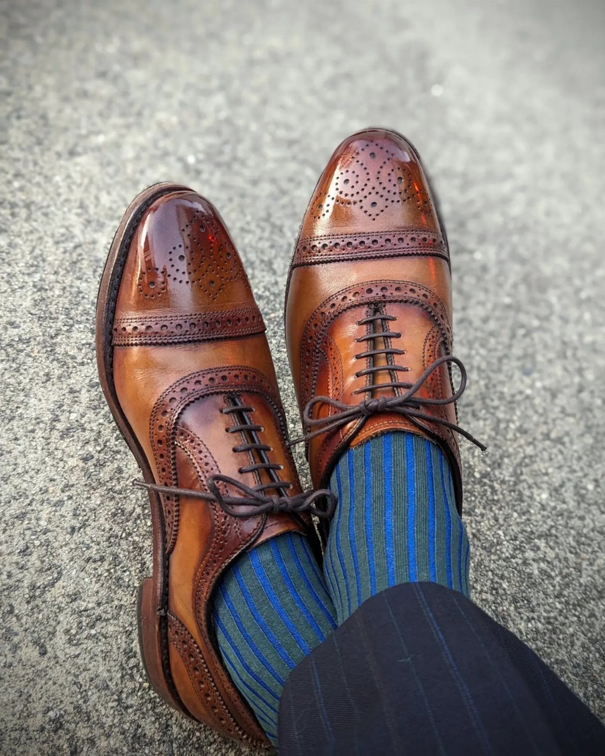 Brown leather brogue oxford shoes paired with blue striped socks and pinstriped trousers.