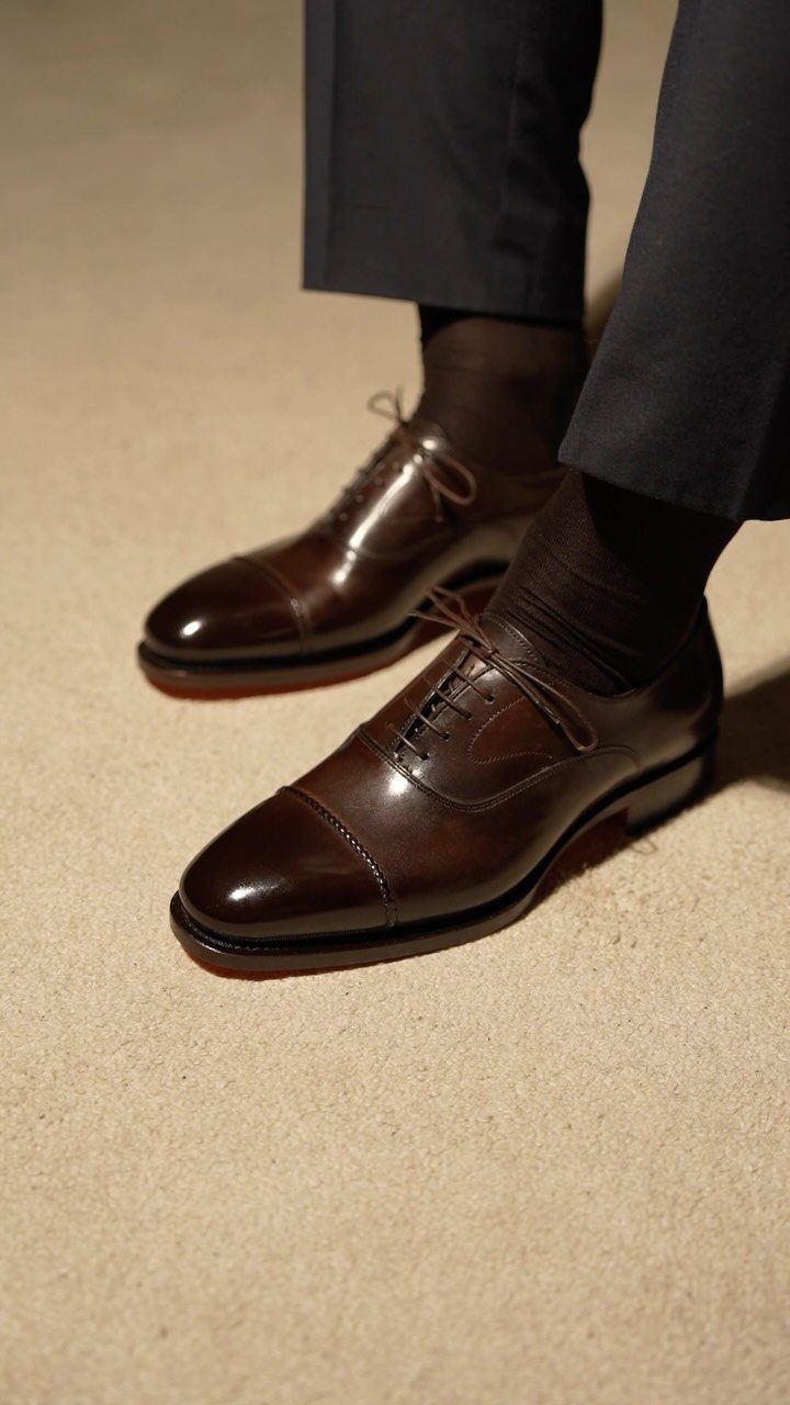Dark brown leather oxford shoes paired with navy blue trousers and brown socks.