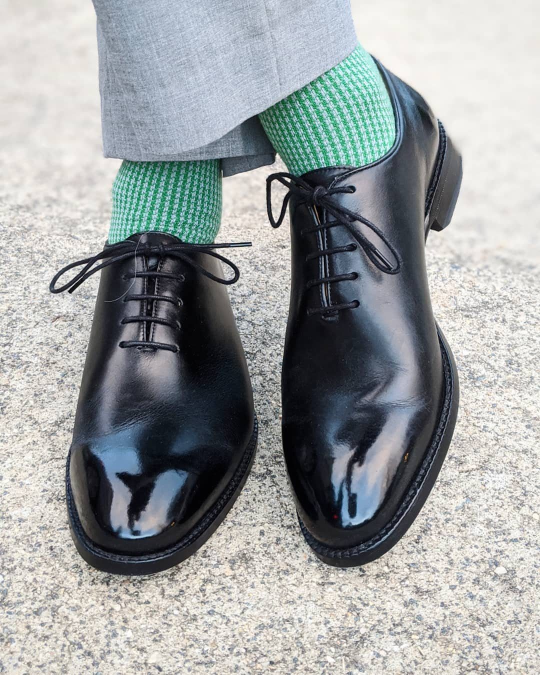 Polished black leather oxford shoes with bright green socks and grey trousers.