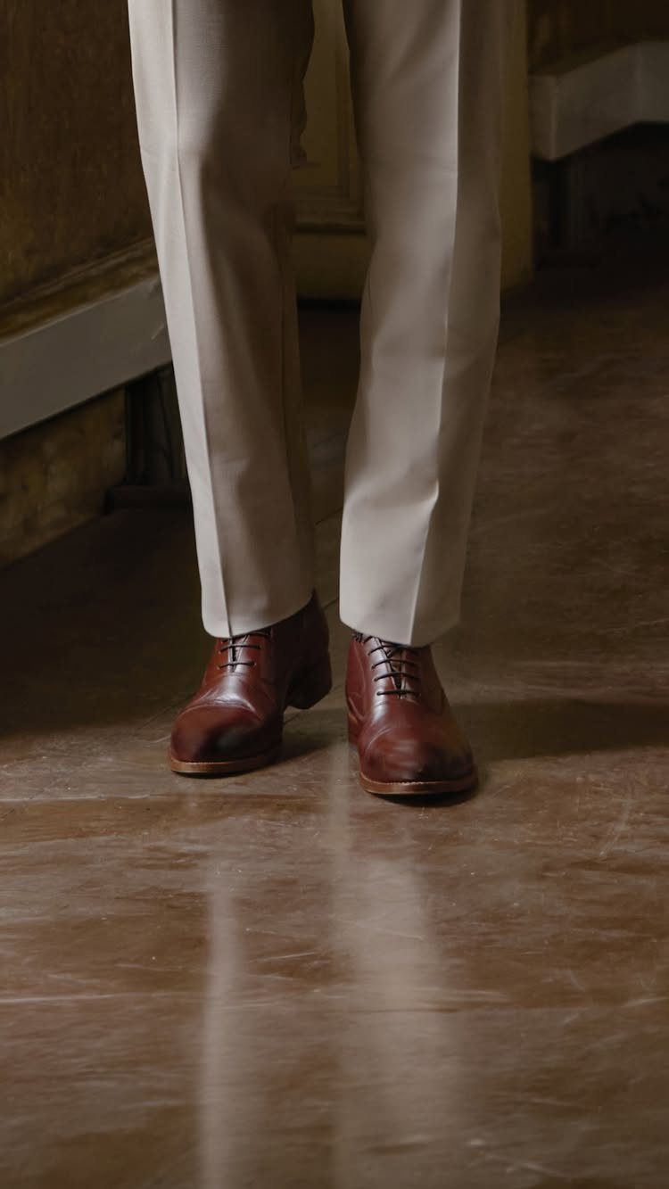 Brown leather oxford shoes paired with beige trousers on a wooden floor