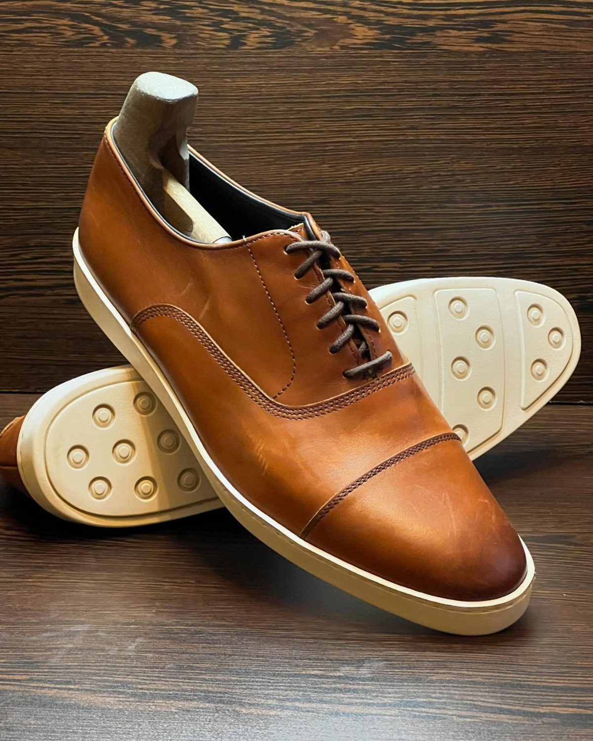 Tan leather oxford shoes with white soles on a dark wooden background.