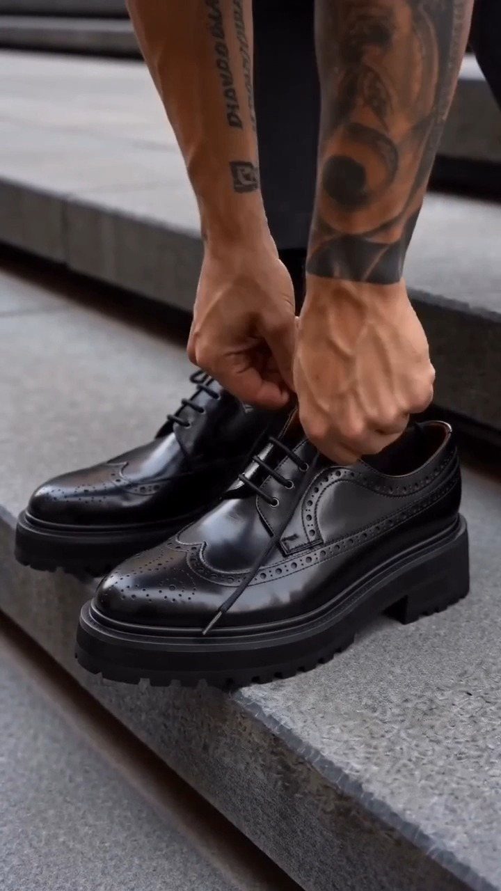 Black leather oxford shoes with thick soles being tied on stone steps.