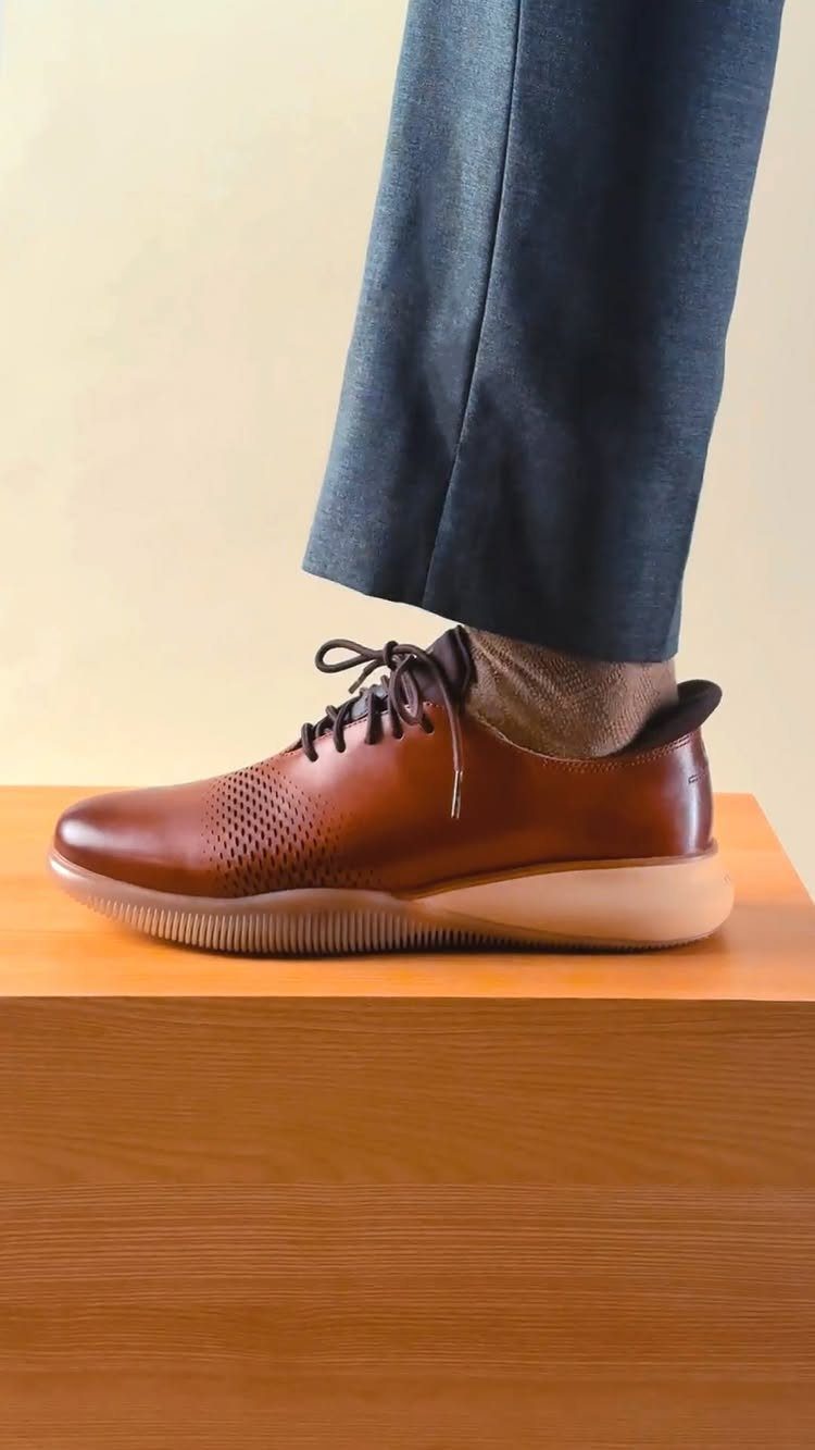 Brown leather oxford shoes with flexible rubber soles and grey dress trousers.