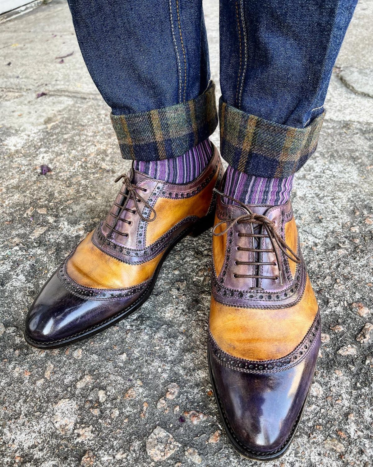 Two-tone leather oxford shoes paired with cuffed blue jeans and purple striped socks.