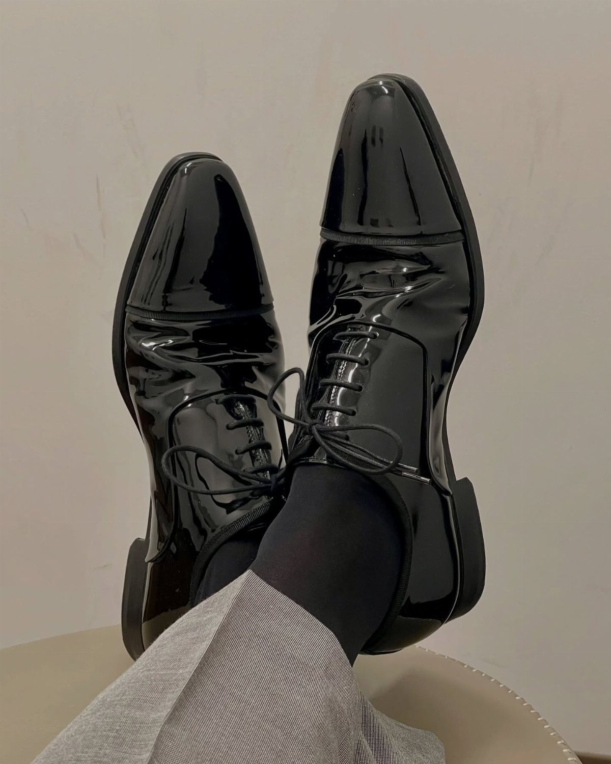 Black patent leather oxford shoes worn with grey trousers and black socks.