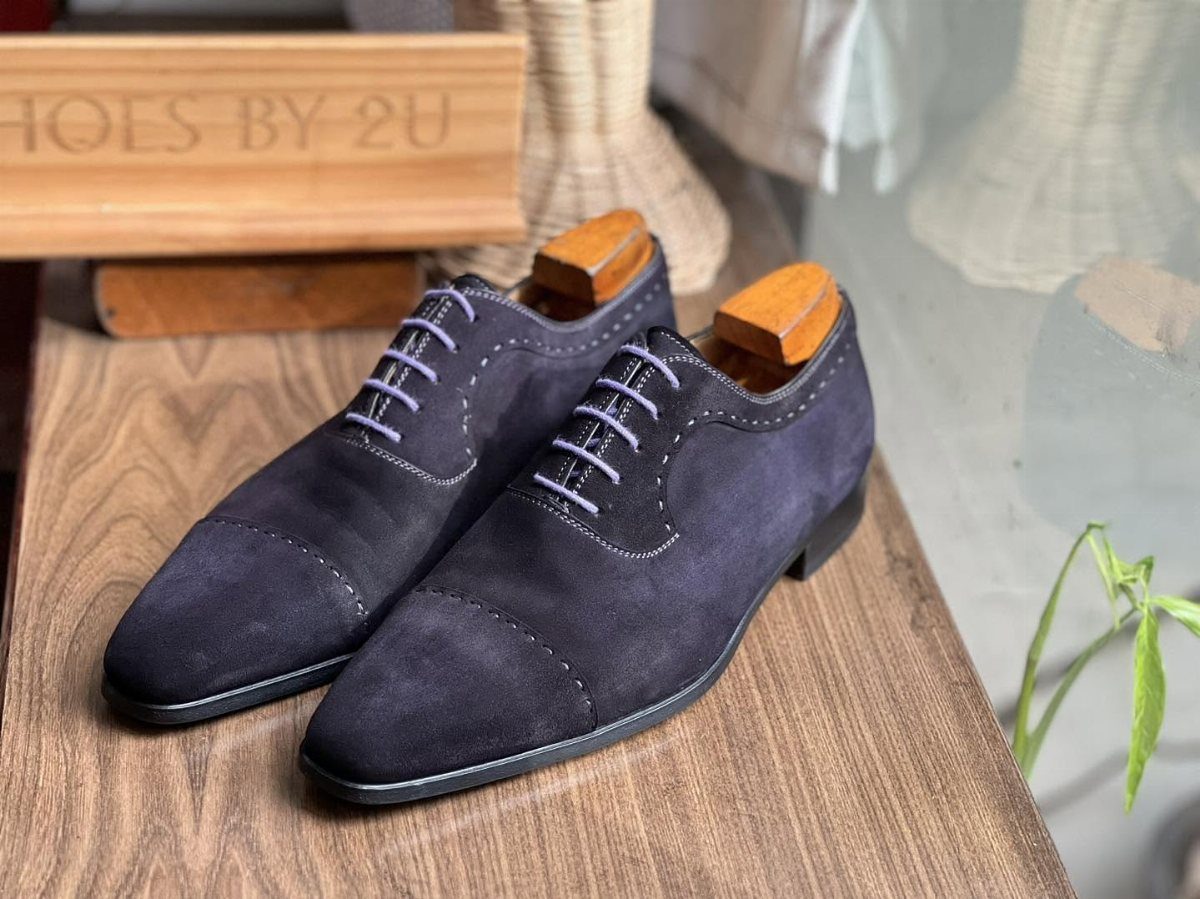 Dark navy blue suede oxford shoes with cap toes on a wooden table