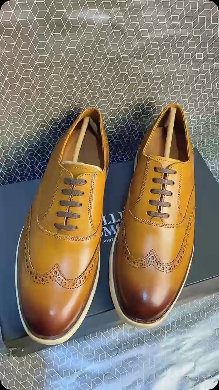 Tan leather wingtip oxford shoes resting on a blue shoebox with hexagonal background
