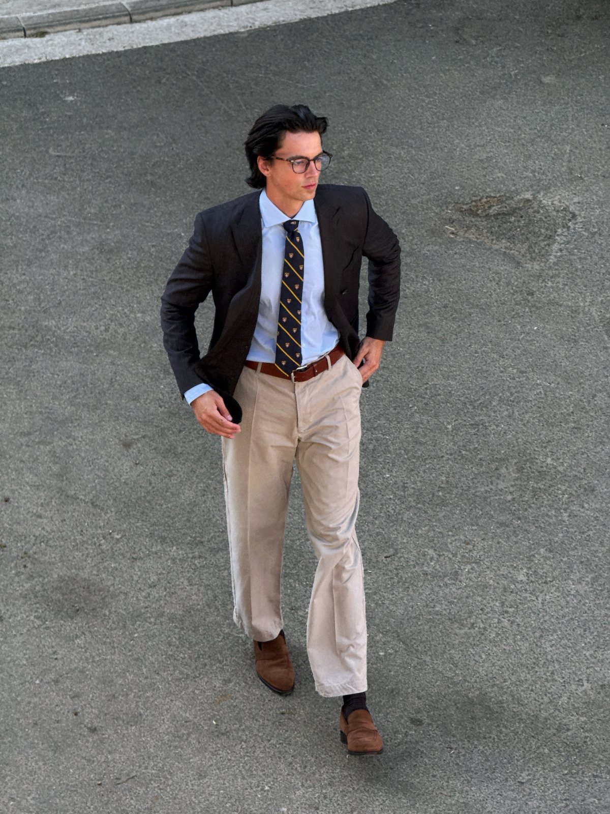 Man in brown blazer and beige trousers wearing brown suede loafers walking outdoors.