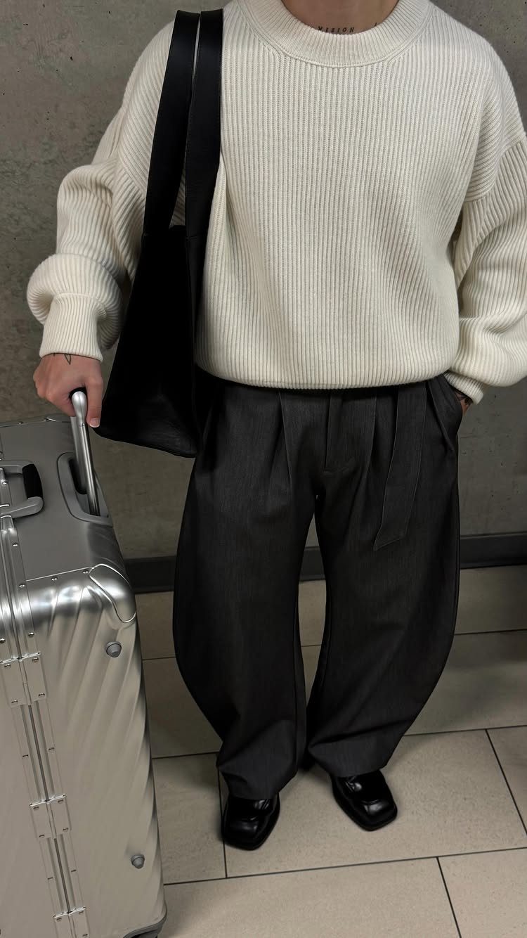 Person wearing a cream sweater, grey pleated trousers, and black leather penny loafers.