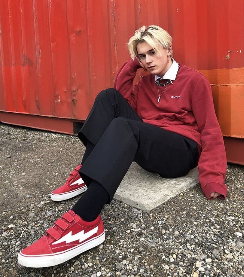 Young man in red sweatshirt and black trousers wearing red and white sneakers.