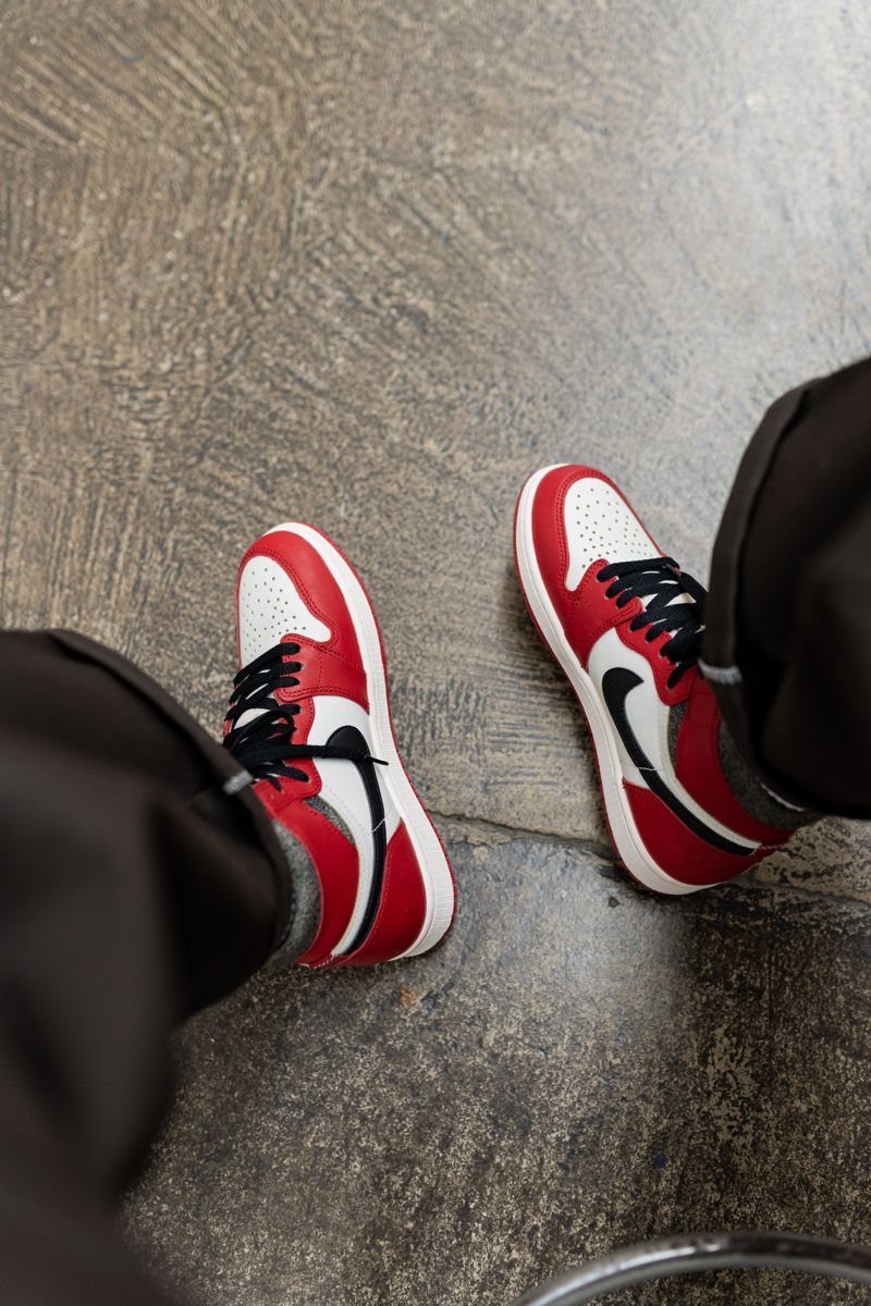 Red and white sneakers paired with dark charcoal grey trousers on concrete floor