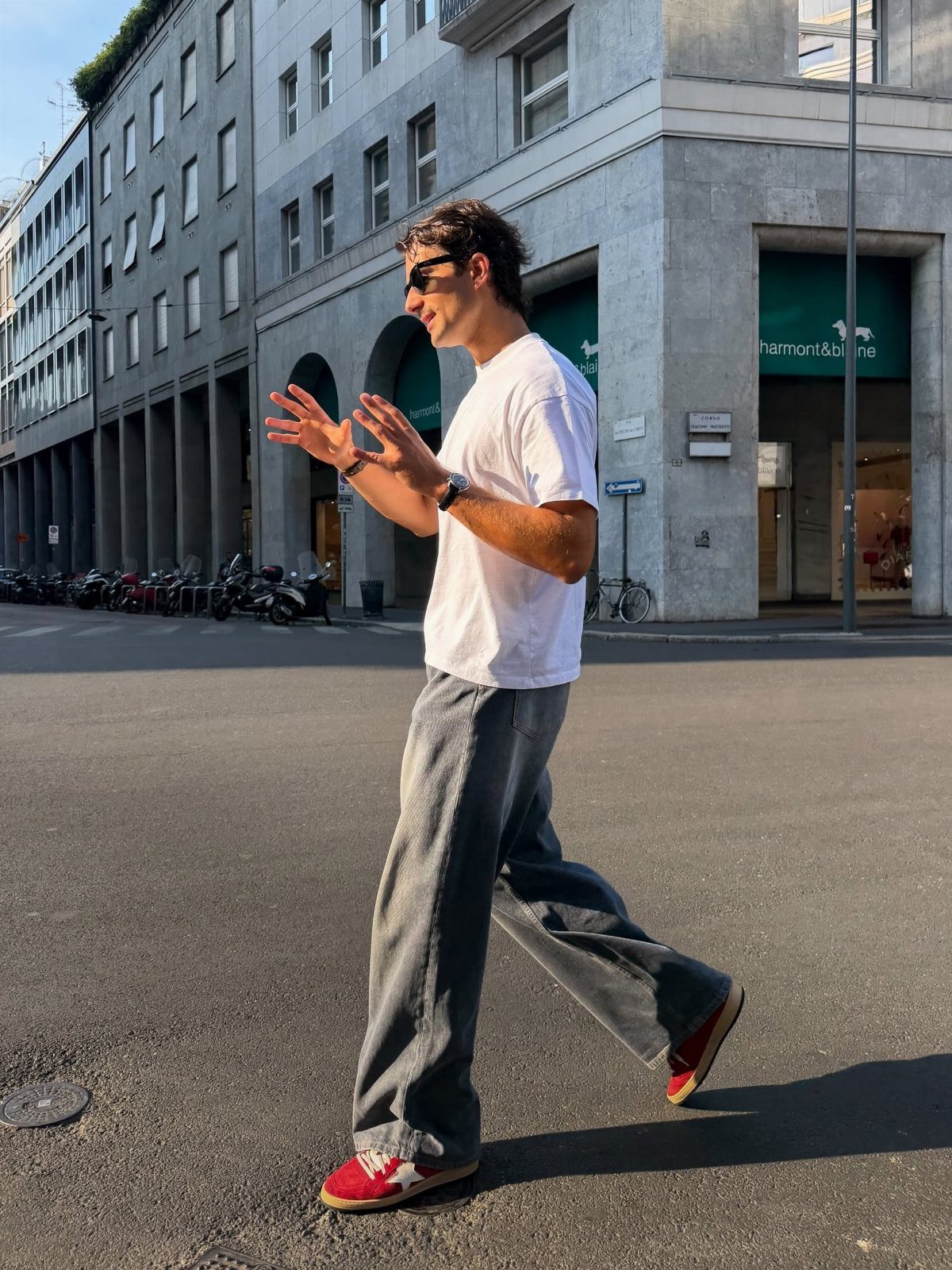 Man walking in grey wide-leg jeans and red and white sneakers on city street