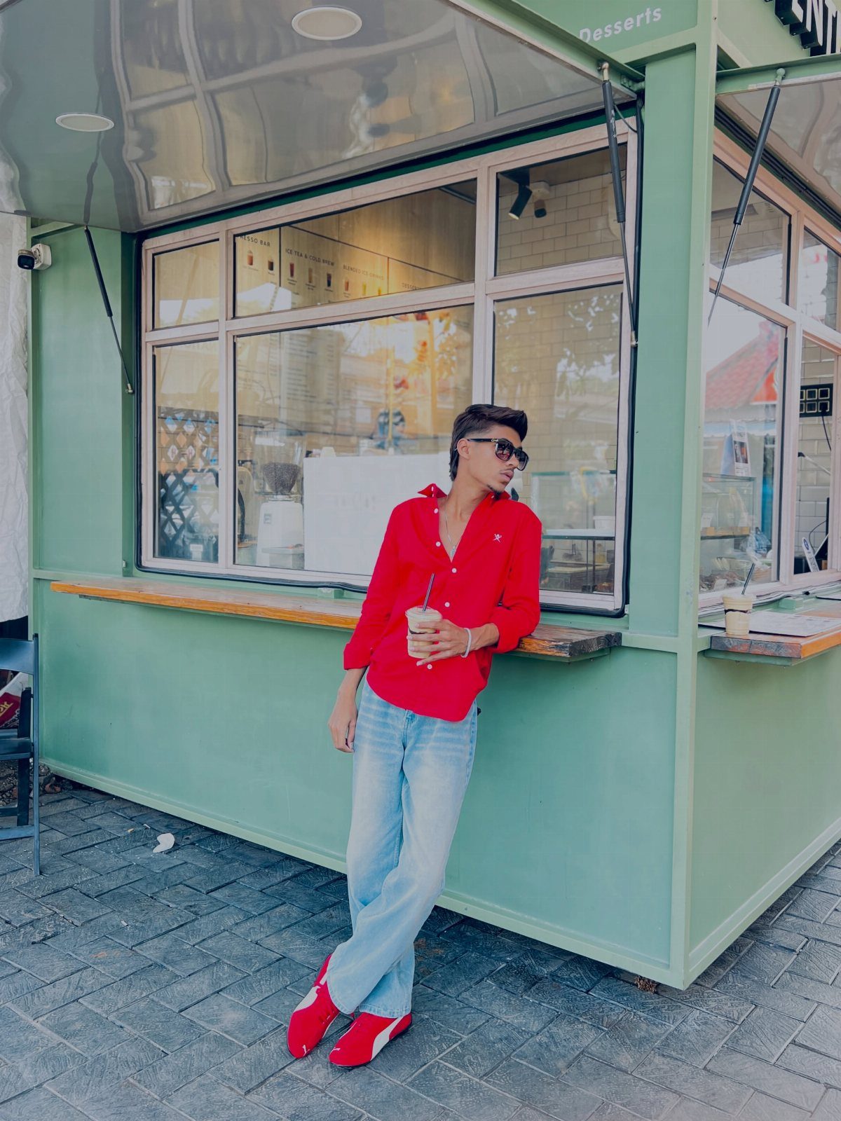 Man in red shirt and light blue jeans wearing red sneakers by a kiosk