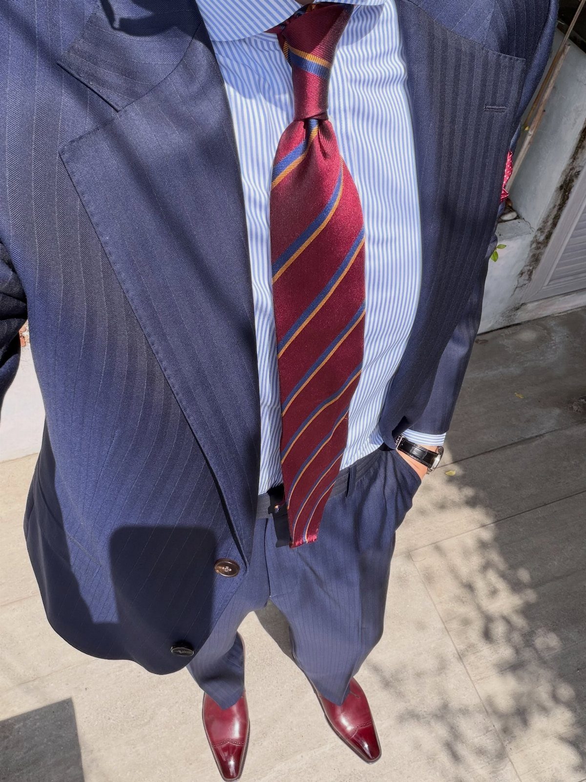 Man in navy blue suit and red striped tie wearing dark red dress shoes