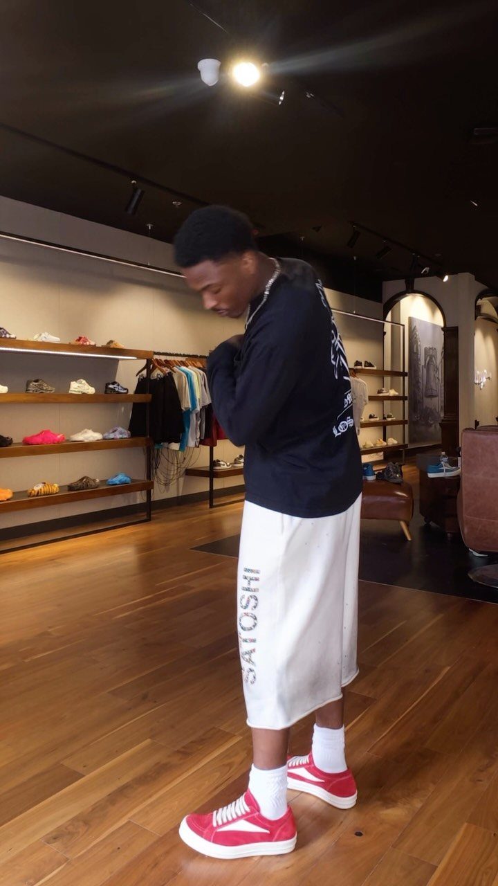 Man wearing red sneakers, white shorts, and a black shirt in a shoe store.