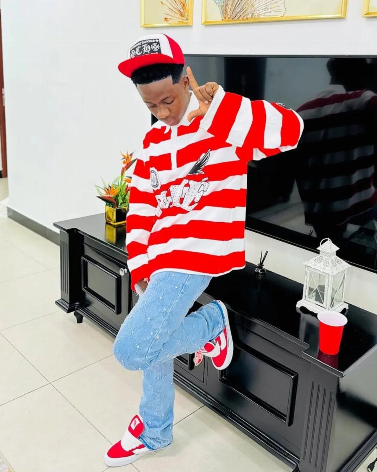 Man in red and white striped shirt, blue jeans, and red sneakers posing indoors.