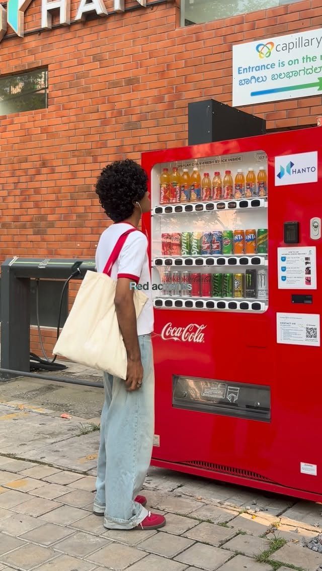 Man in white t-shirt and light blue jeans wearing red shoes by vending machine