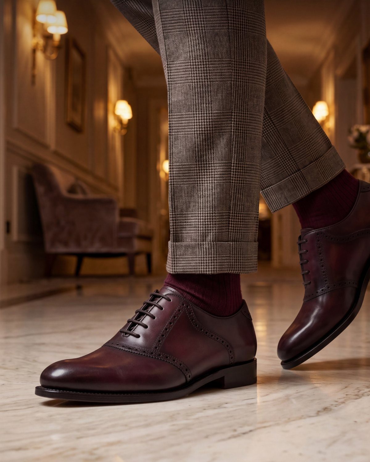 Dark red leather dress shoes paired with grey patterned trousers and burgundy socks.