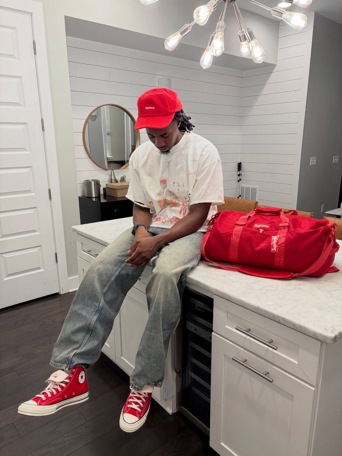 Man in red sneakers, blue jeans, and red cap sitting on kitchen counter