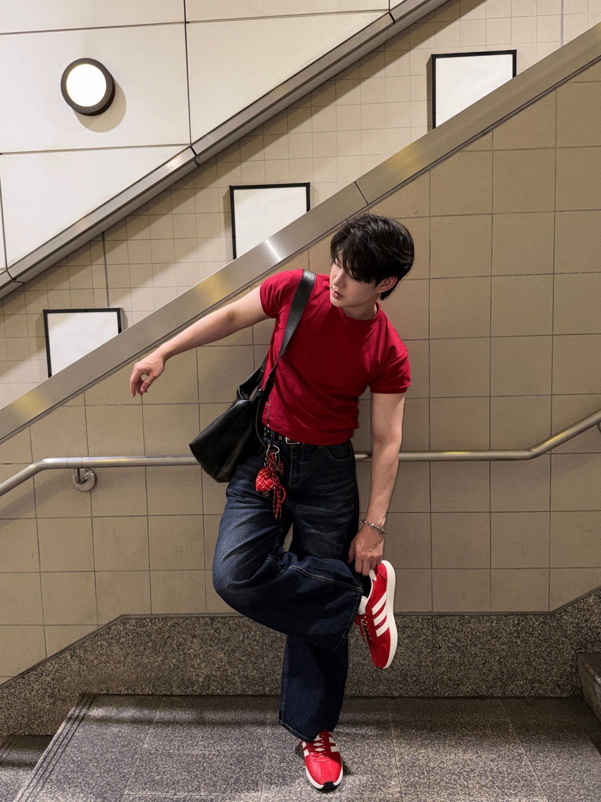 Man in red t-shirt and blue jeans wearing bright red sneakers on stairs