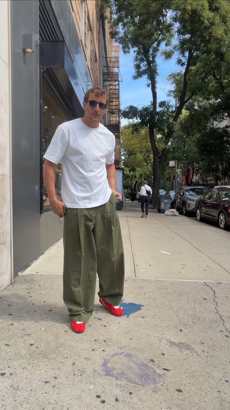 Man in white t-shirt and olive trousers wearing bright red shoes on sidewalk