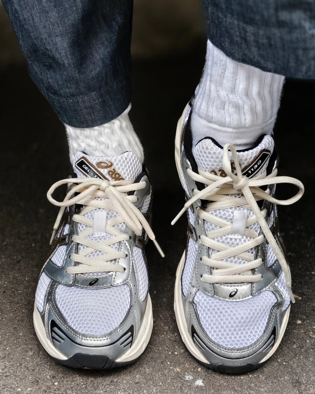 Silver and white ASICS Gel 1130 sneakers worn with white socks and blue jeans.
