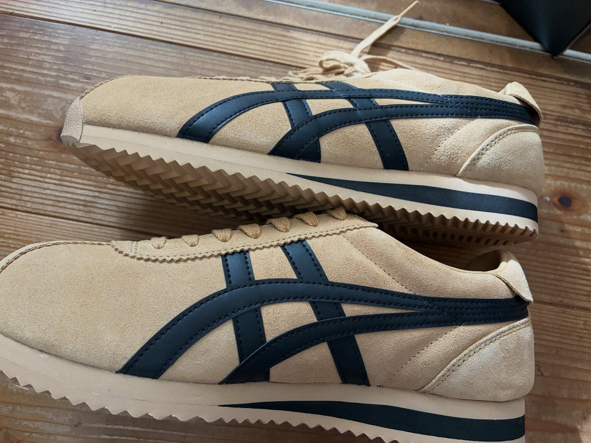Tan suede running shoes with navy blue stripes on a wooden floor.