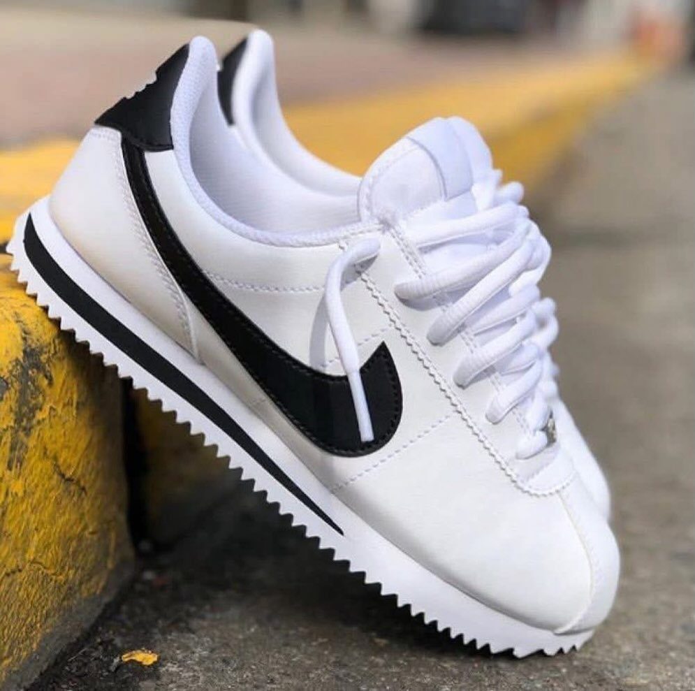 White Nike Cortez sneakers with black swoosh resting on a yellow concrete curb.