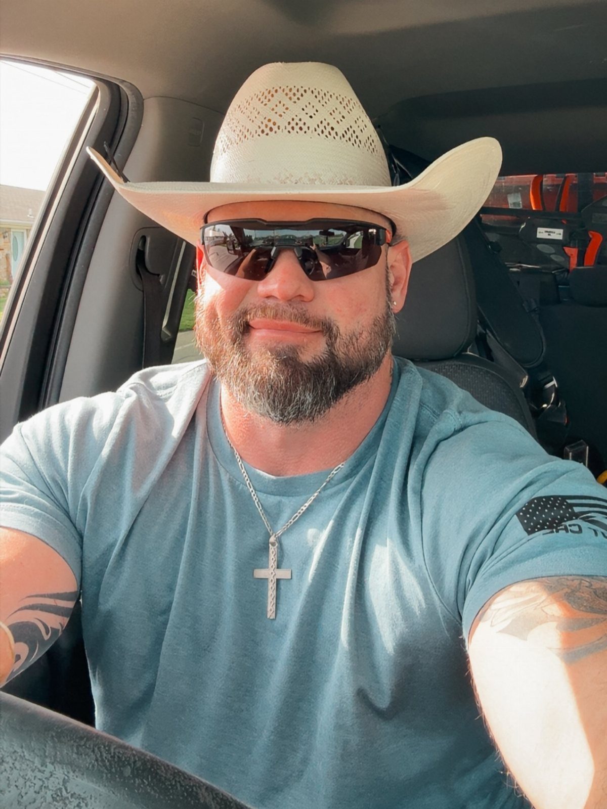 Man with groomed beard wearing a white cowboy hat and sunglasses in a car
