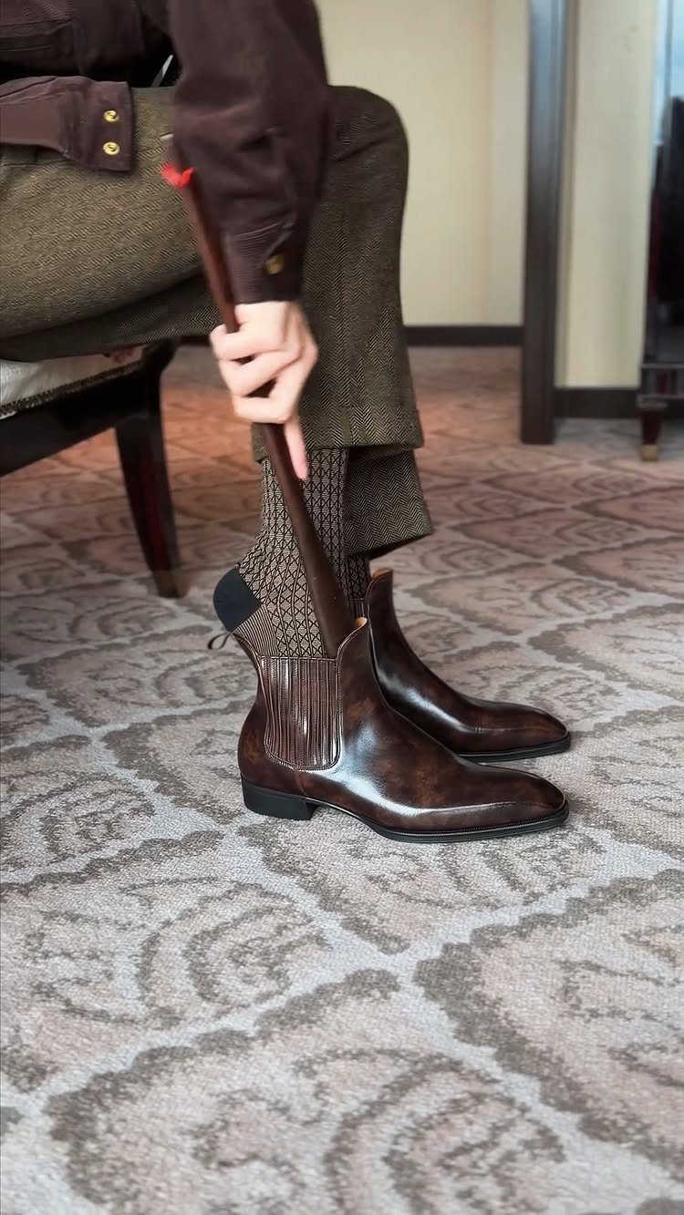 Dark brown leather Chelsea boots being put on with tweed trousers and socks.
