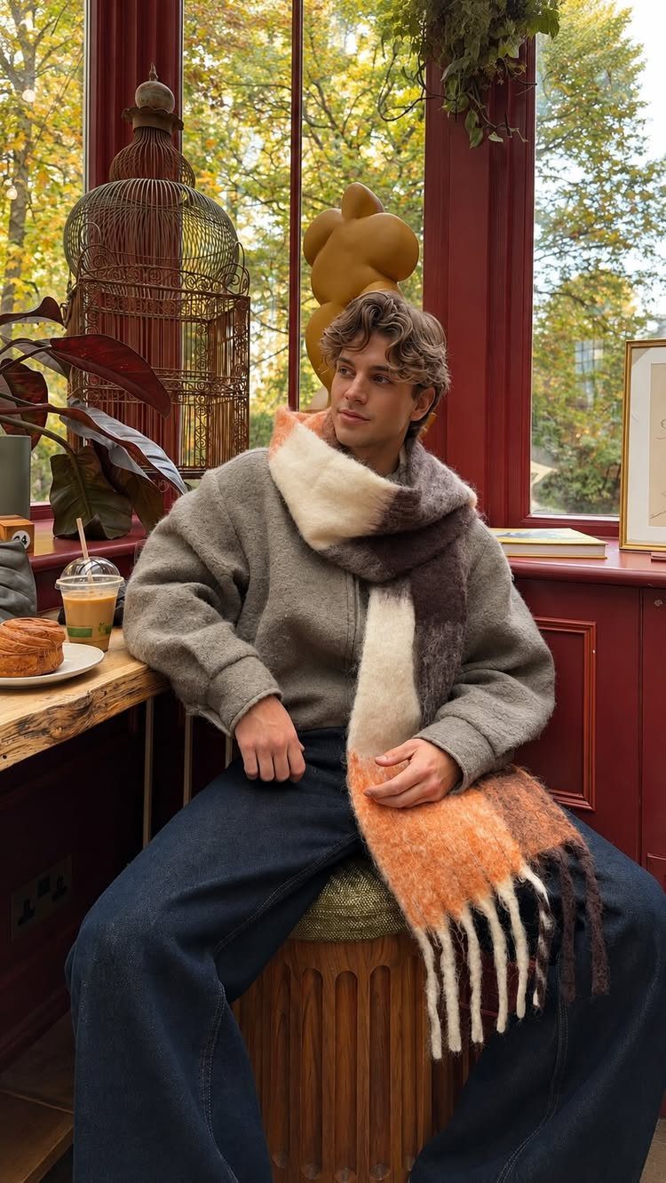 Man wearing a thick multi-colored scarf and grey sweater sitting in a cafe