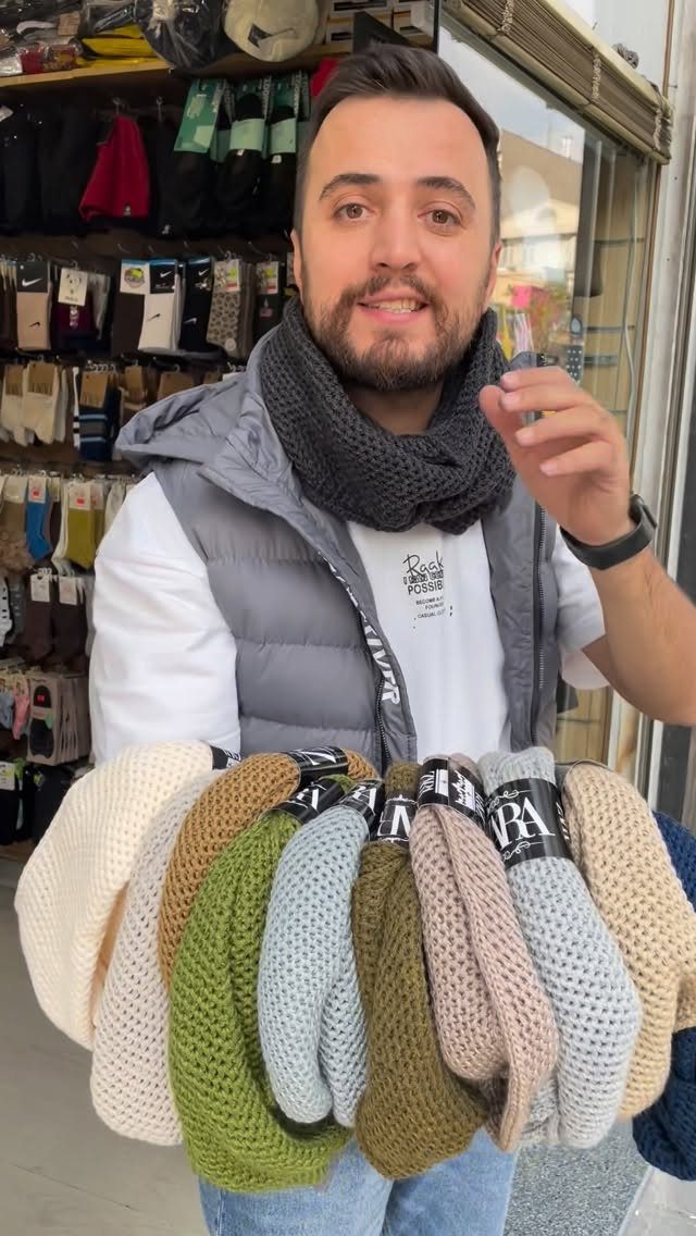 Man wearing a grey infinity scarf holding several colorful knit scarves in a store