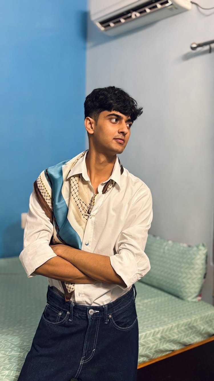 Young man wearing a white shirt and blue jeans with a patterned scarf.