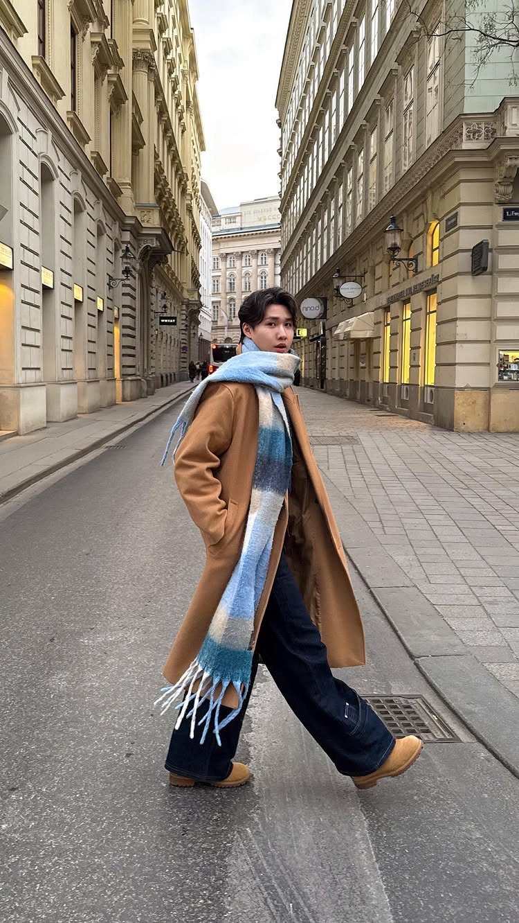 Man in tan coat and blue checkered scarf walking on a city street