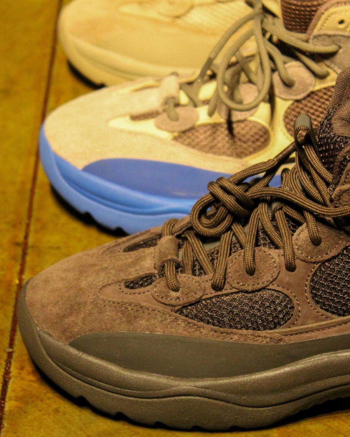 Brown suede sneakers and beige sneakers with blue soles on a wooden floor