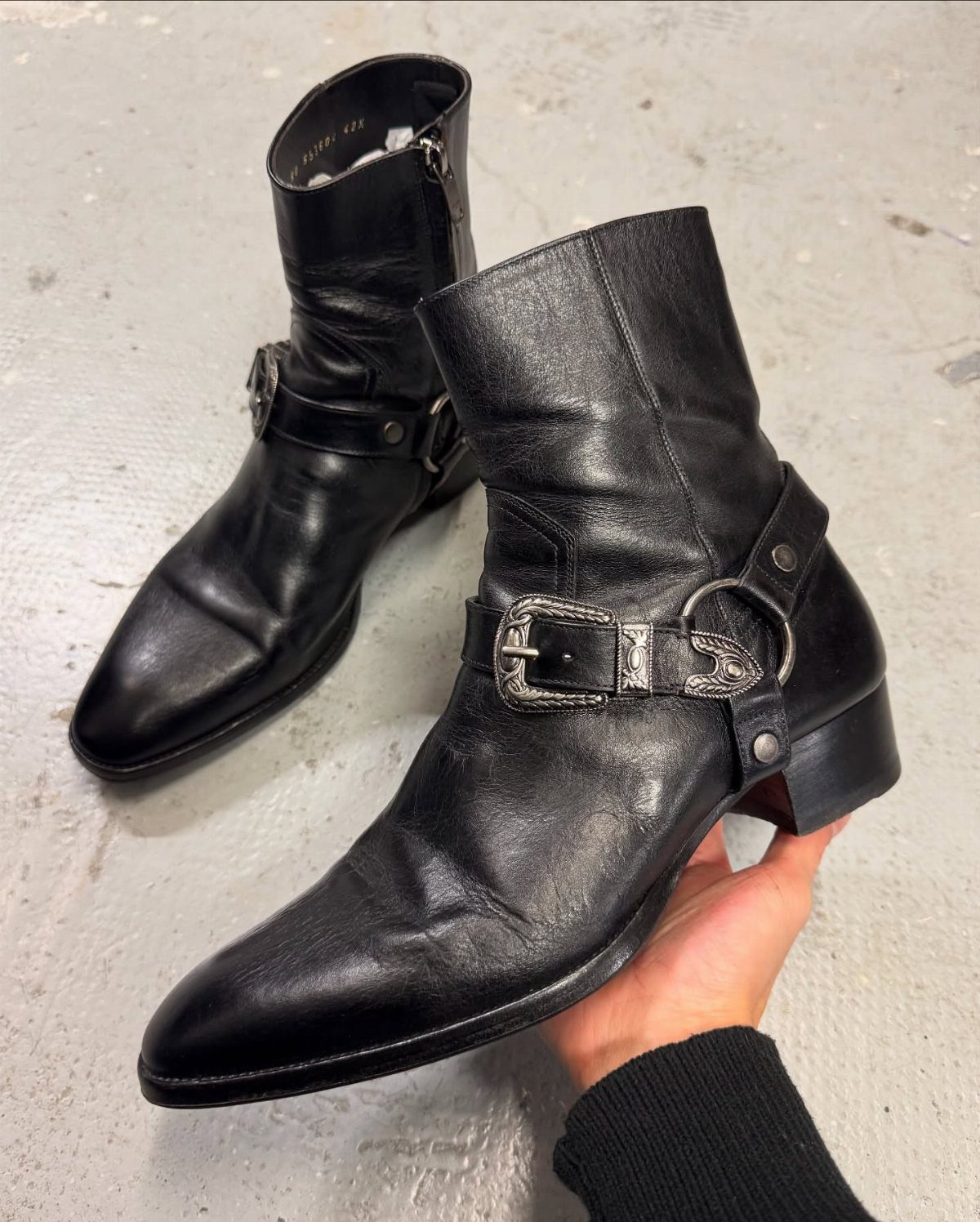 Black leather ankle boots with silver buckle straps on a concrete floor
