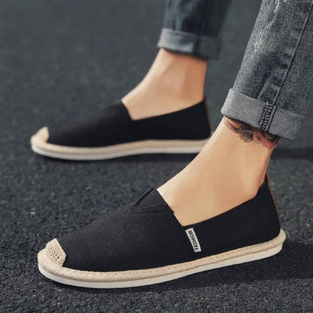 Black canvas slip-on espadrilles with white soles worn with cuffed grey jeans.