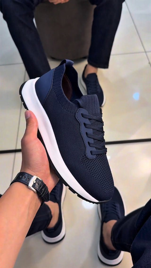 Navy blue knit sneakers with white soles held up by a man.