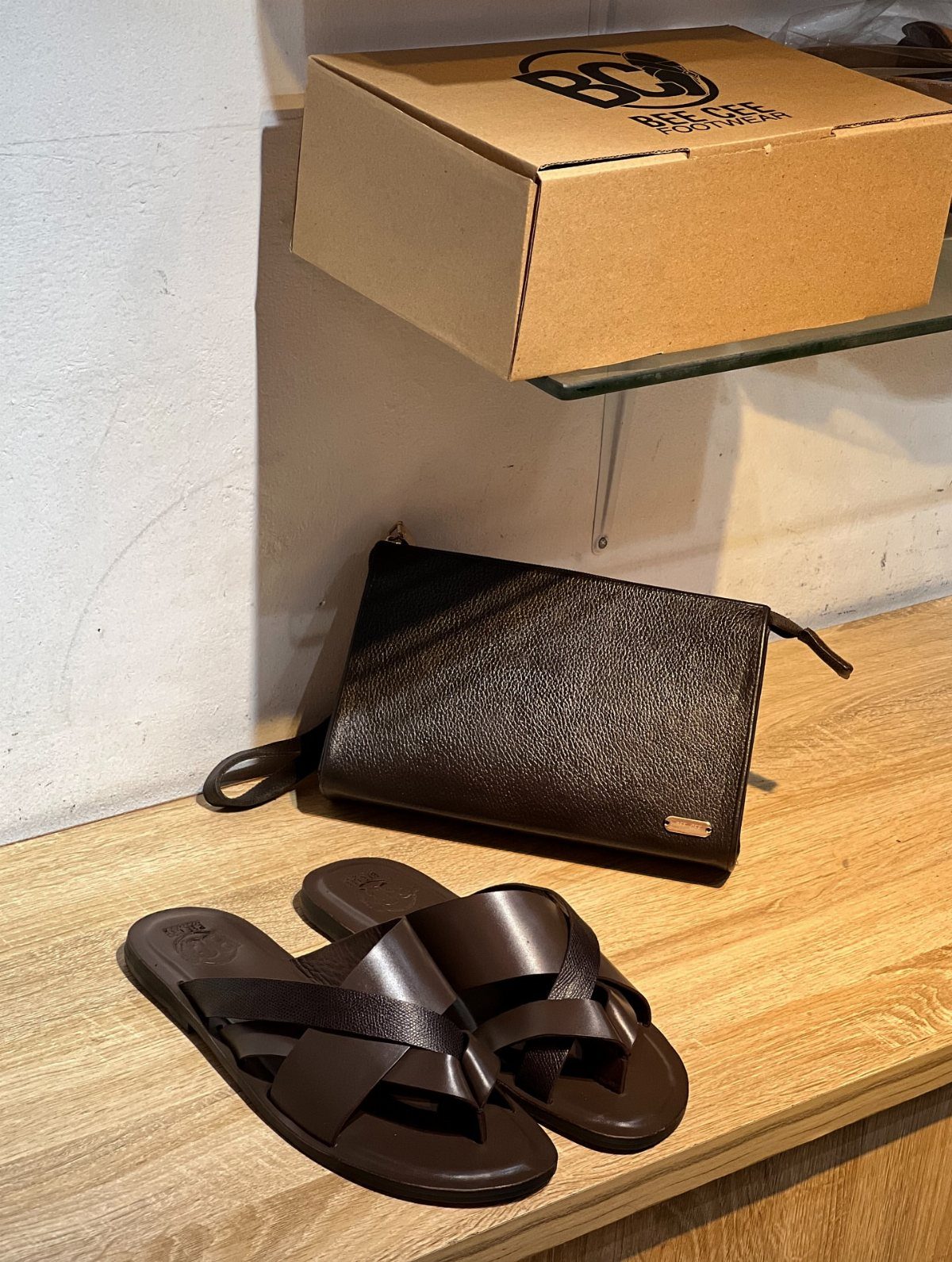 Dark brown leather criss-cross strap sandals next to a leather clutch bag.