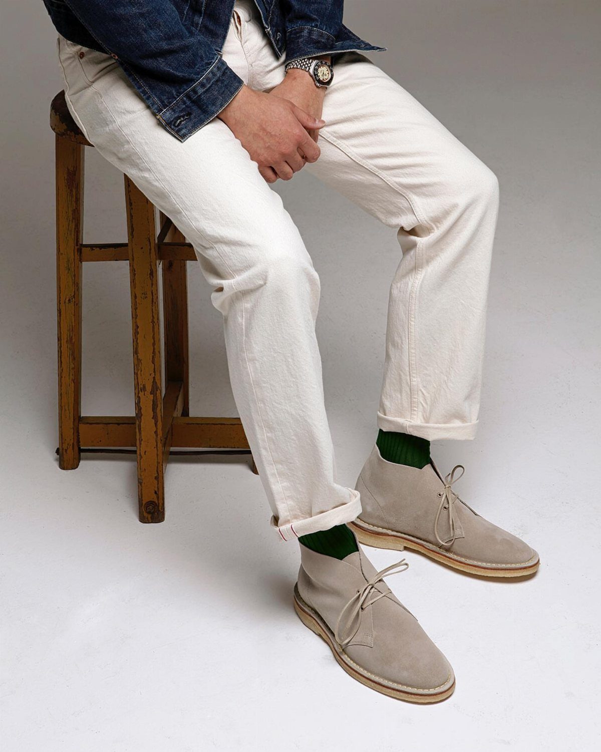 Beige suede chukka boots worn with off-white trousers and dark green socks.