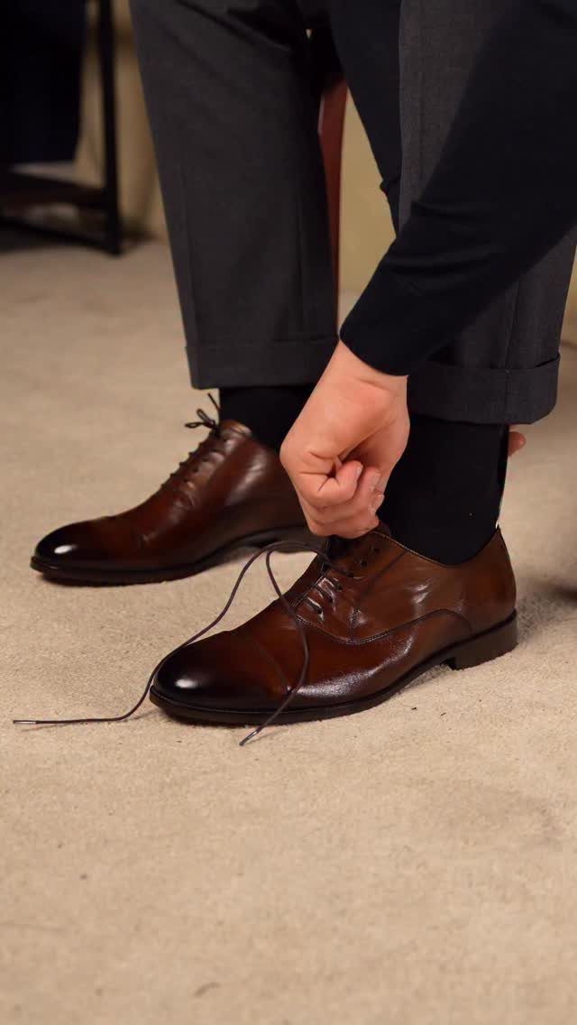 Brown leather derby shoes worn with dark grey suit trousers on a carpet.
