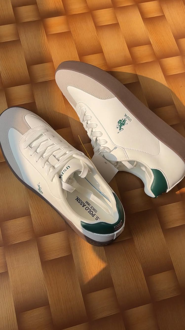 White leather sneakers with green heel accents on a wooden parquet floor