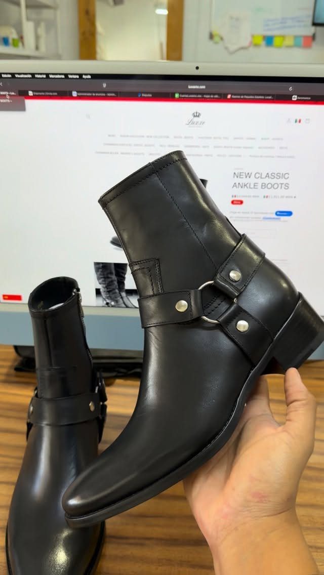 Black leather ankle boots with silver ring details held in front of a computer